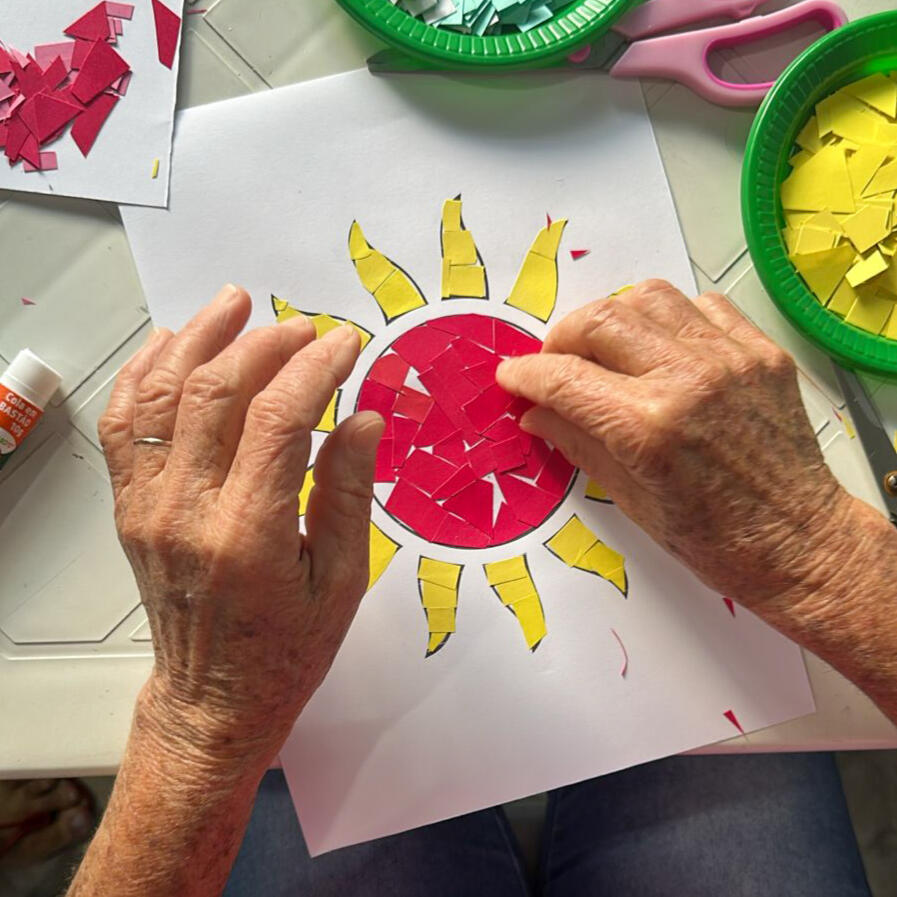 Oficina de Mosaicos em Andamento Idosa fazendo a figura de um sol a partir de recortes